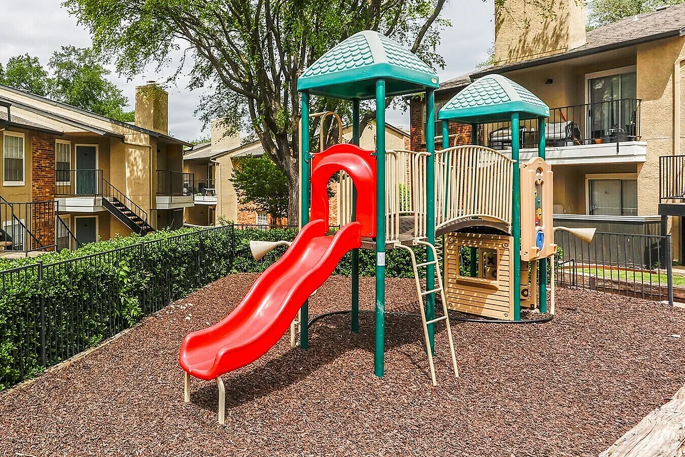 Playground with red slide, turquoise tower structures, wood-chip surfacing, residential buildings