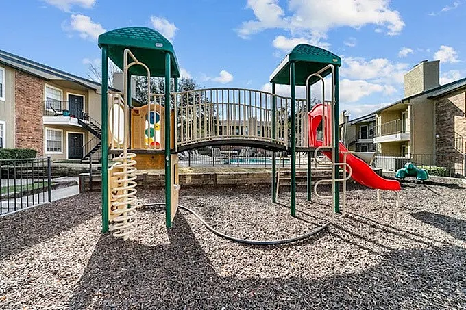 Playground with green canopy structures, climbing walls, red slide, metal bridge walkway