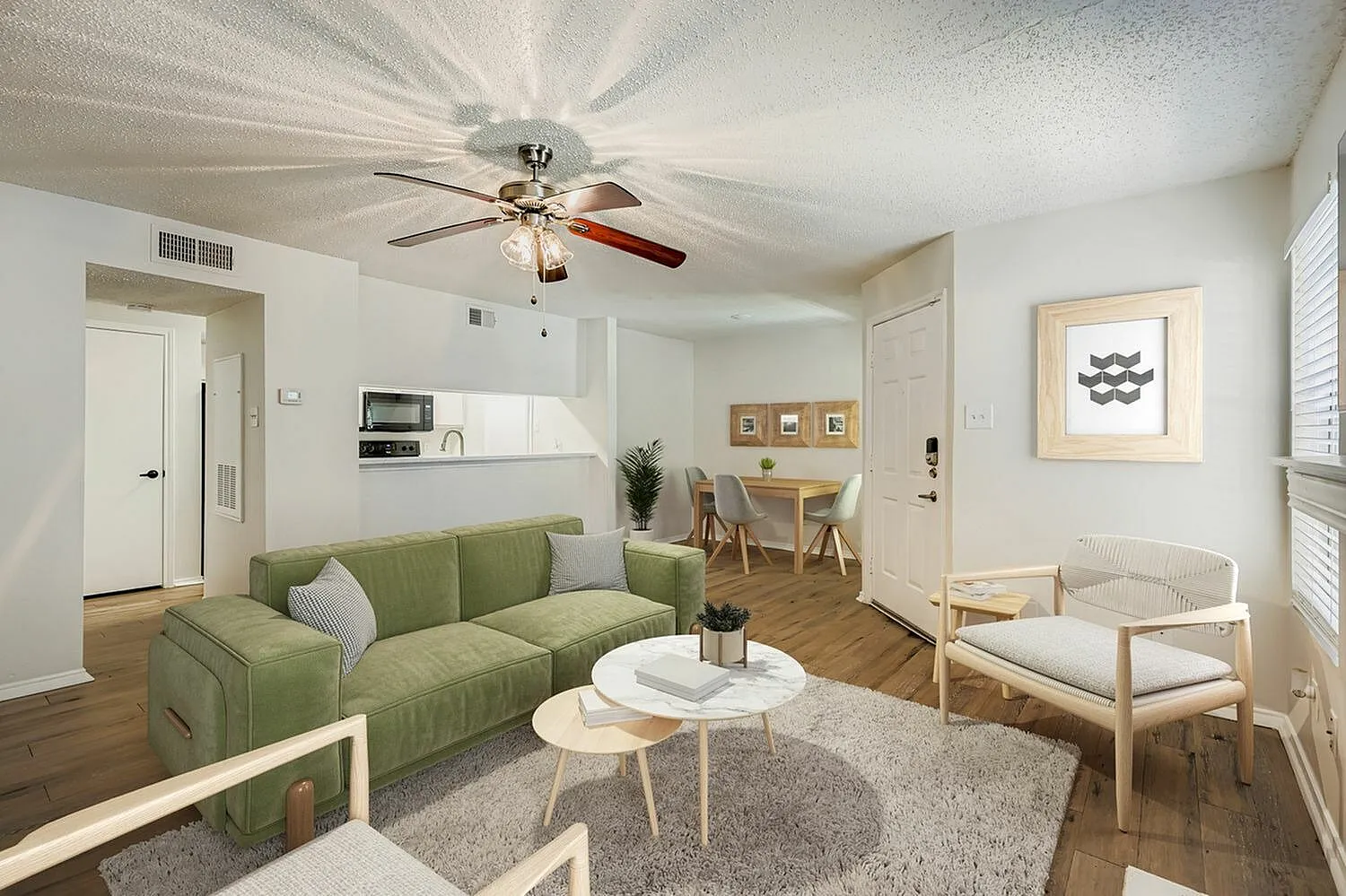Living room with green sofa, wood-style plank flooring, ceiling fan, round coffee table, dining area visible