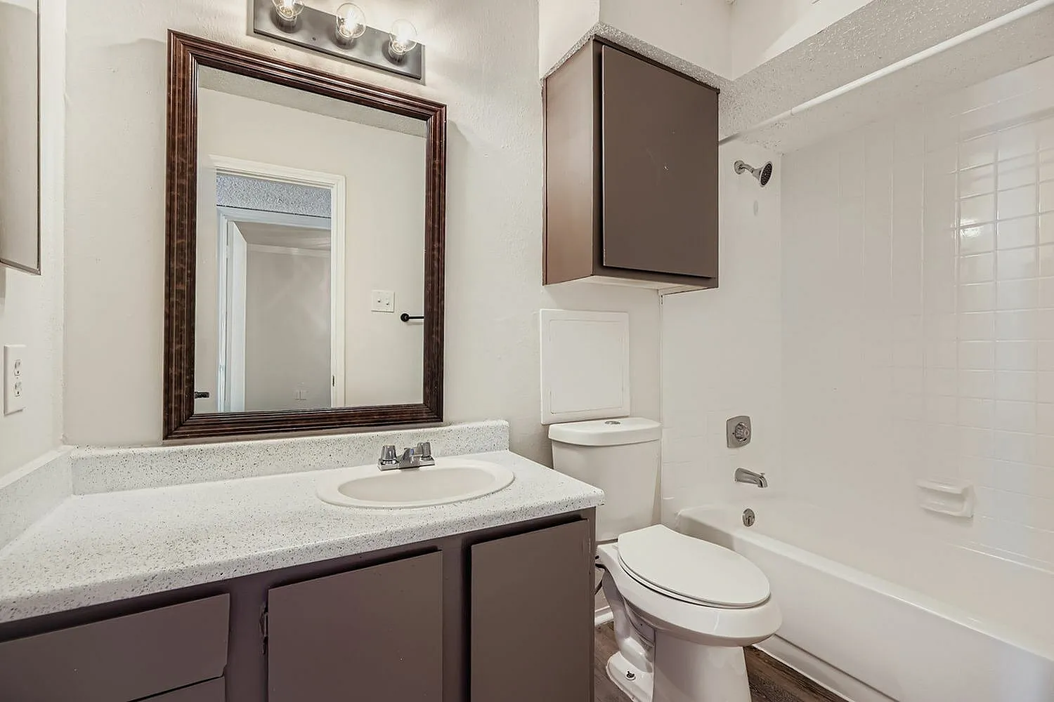 Primary bathroom, dark wood vanity, quartz countertops, framed mirror, tile shower
