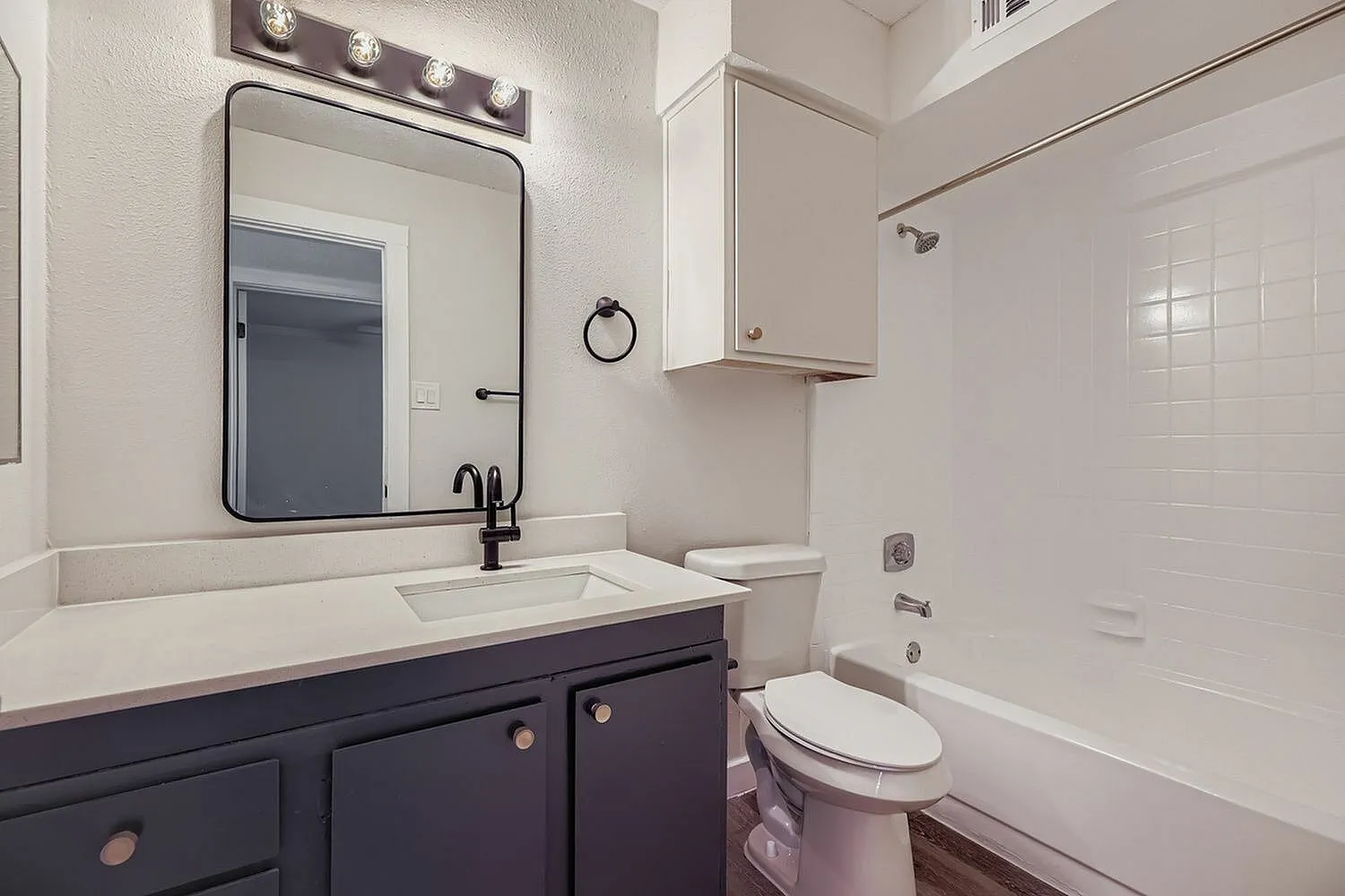 Bathroom, dark shaker vanity, quartz countertop, framed mirror, tub shower combo, wood-style plank flooring