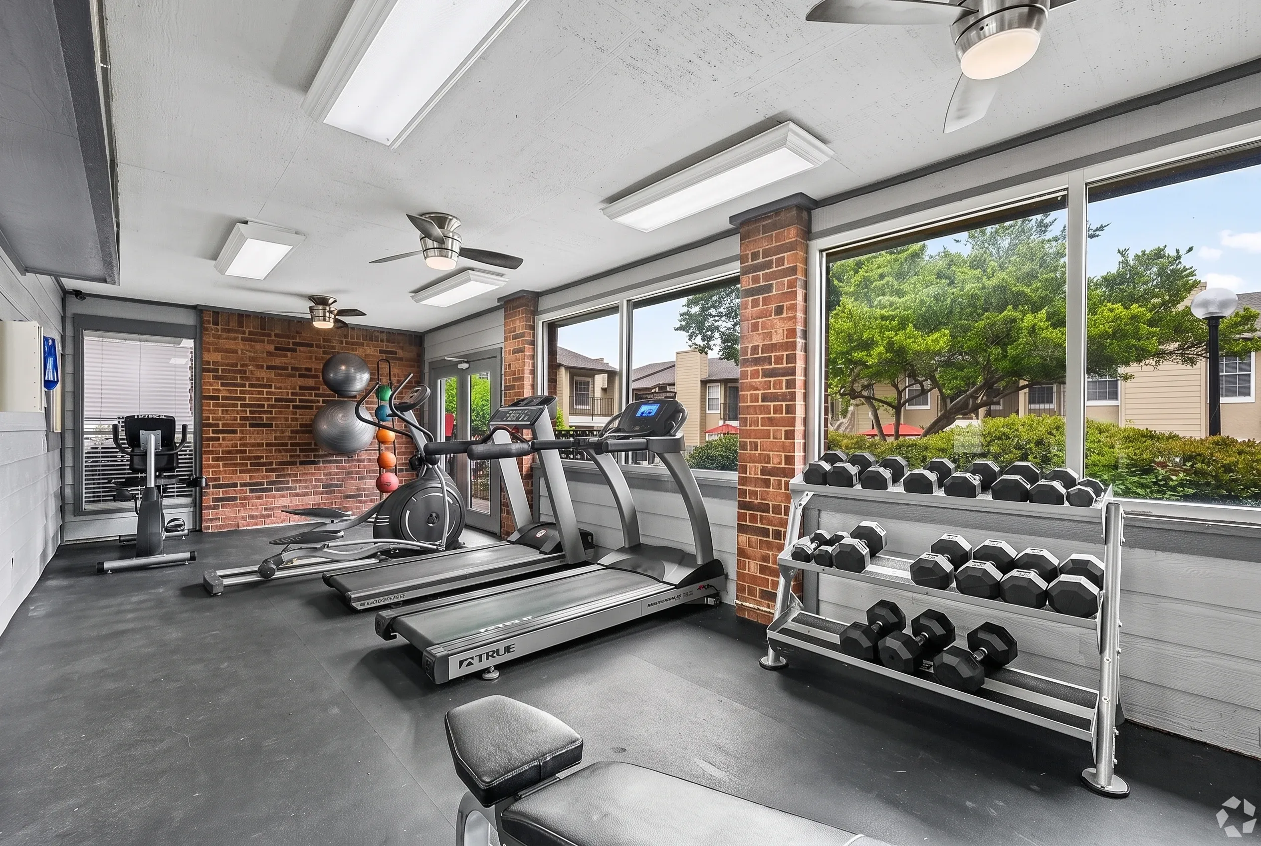 Fitness center, treadmills, ellipticals, dumbbell rack, brick walls, large windows