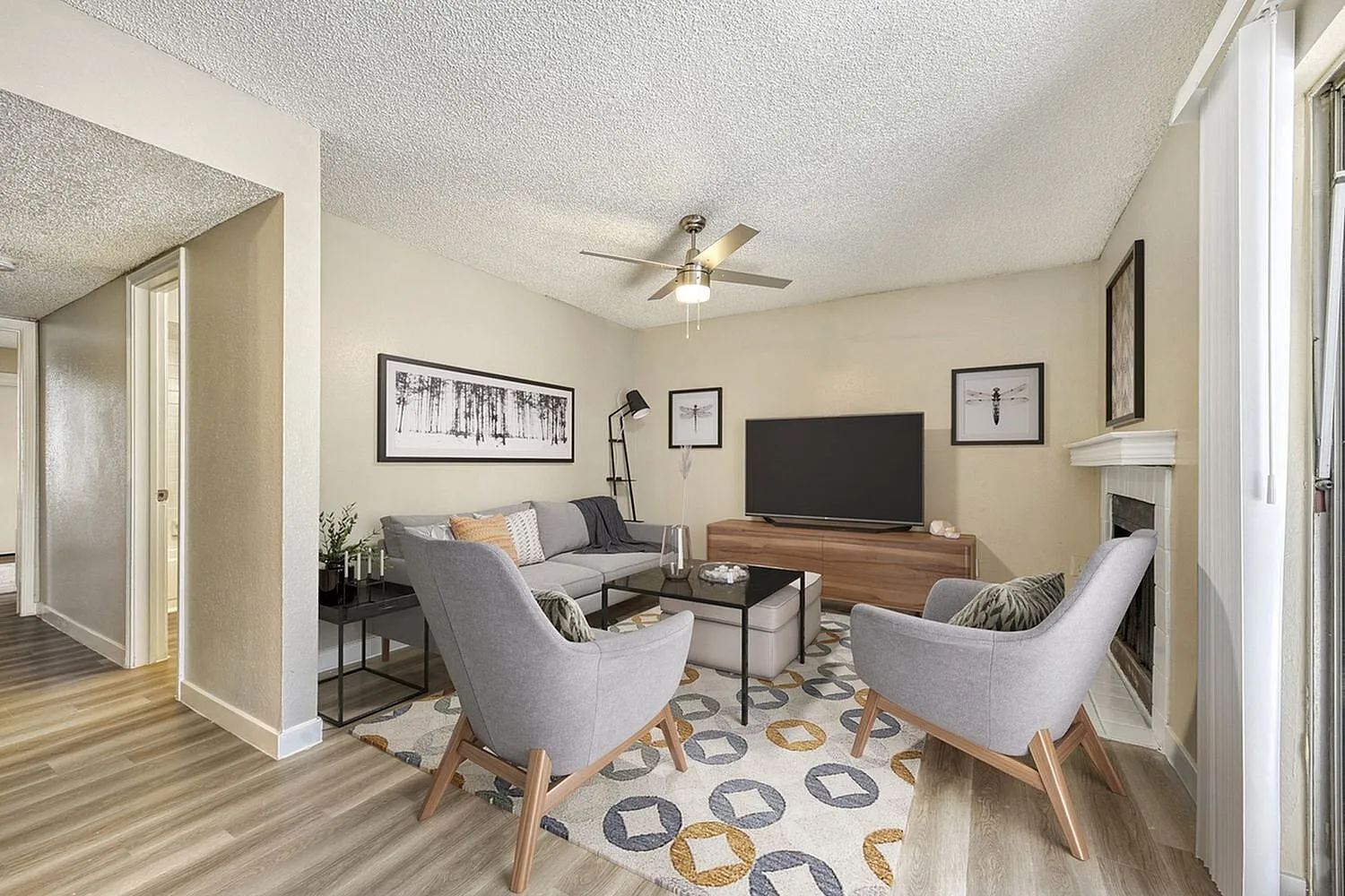 Living room, wood-style plank flooring, gray upholstered chairs, wood television stand, ceiling fan