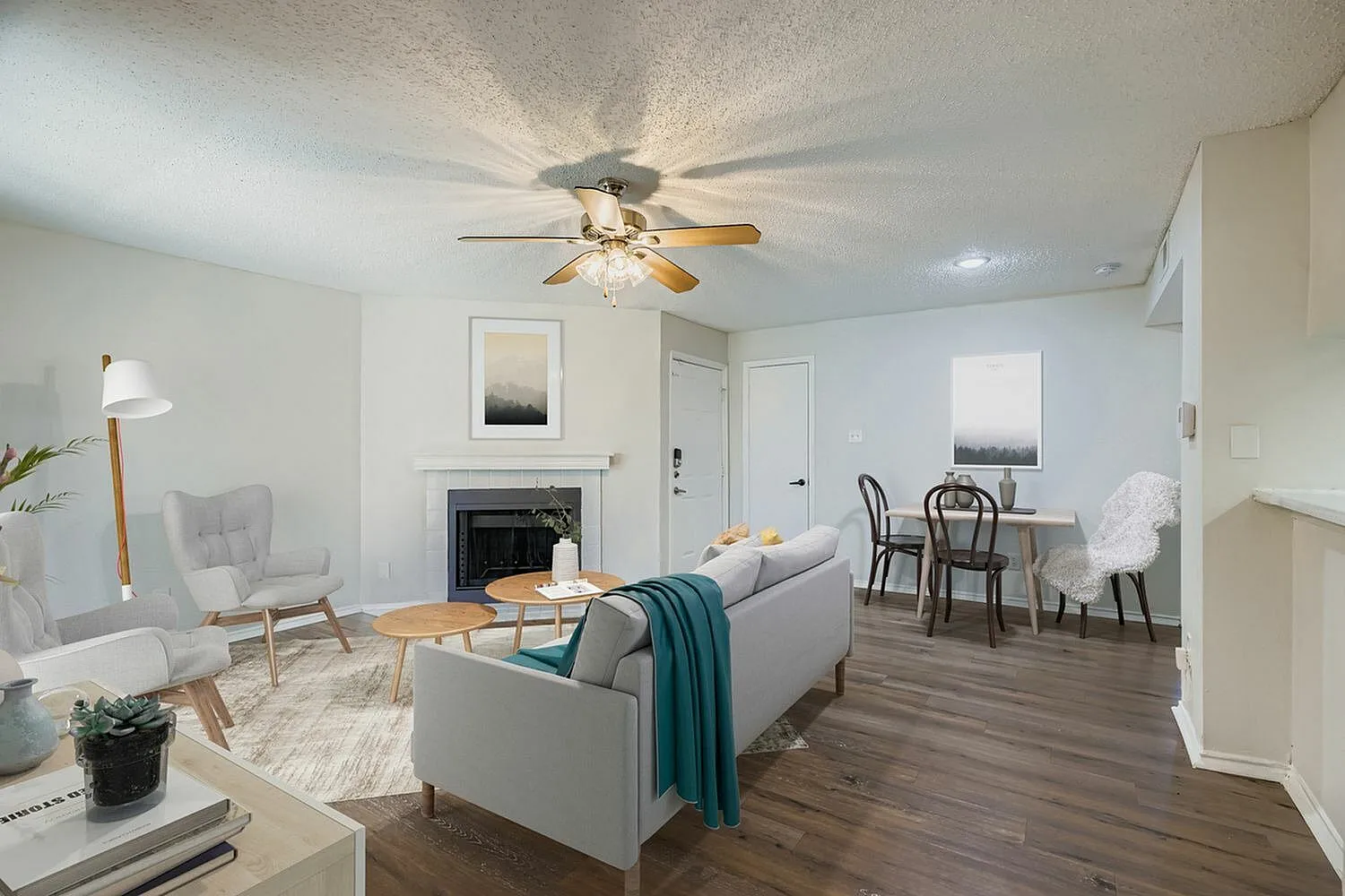 Living room with wood-style plank flooring, ceiling fan, fireplace, gray sofa, dining area