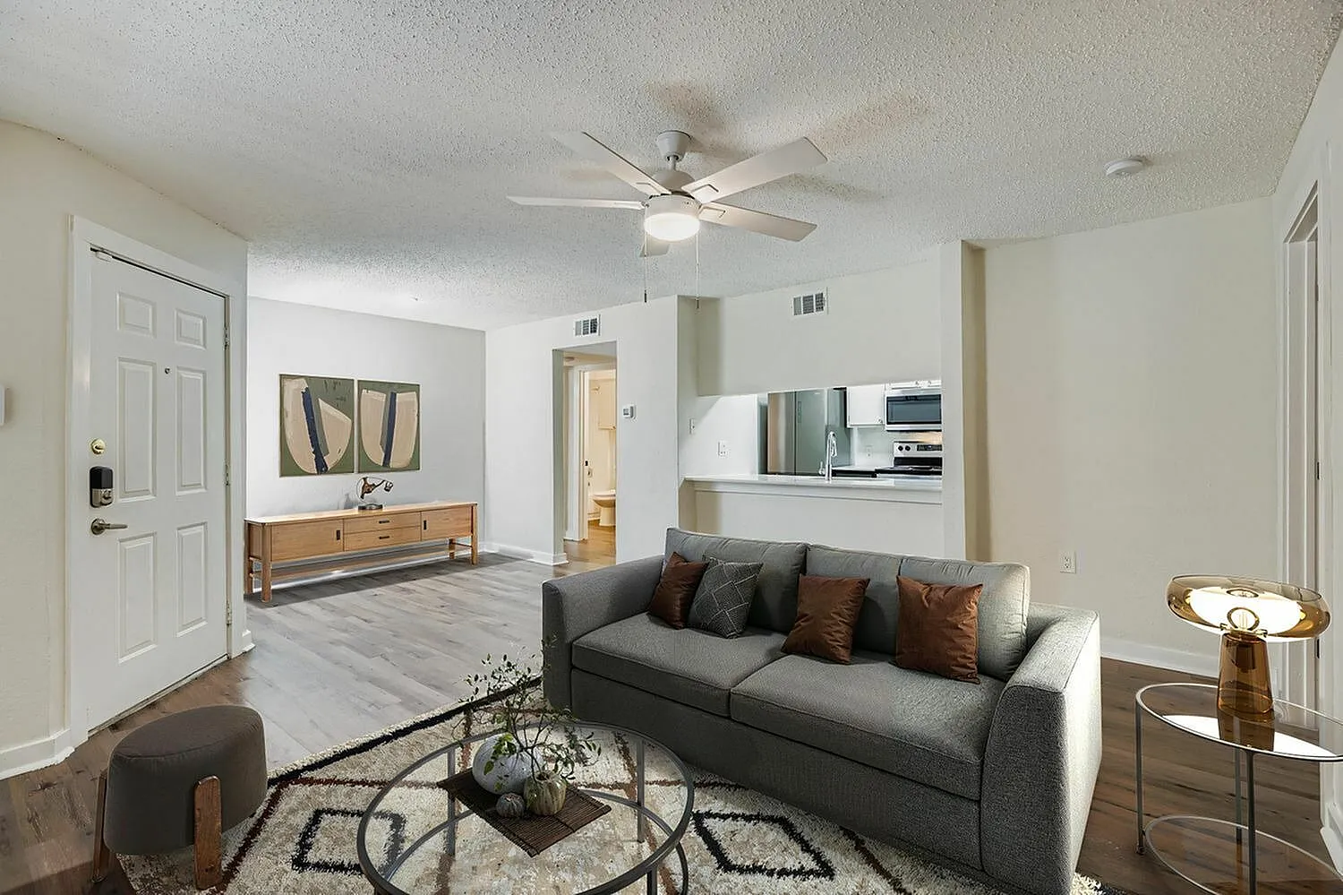 Living room with wood-style plank flooring, dark gray sofa, ceiling fan, geometric area rug