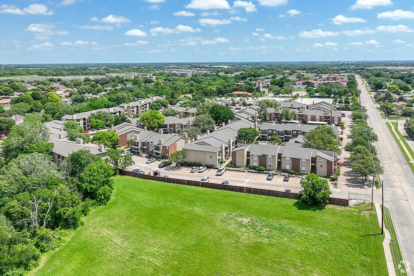 Aerial view of residential community, modern apartment buildings, green open space, mature trees, street access