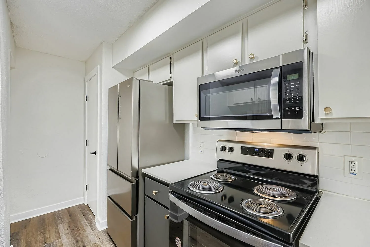 Kitchen, stainless steel appliances, white cabinetry, black electric range, microwave, wood-style plank flooring