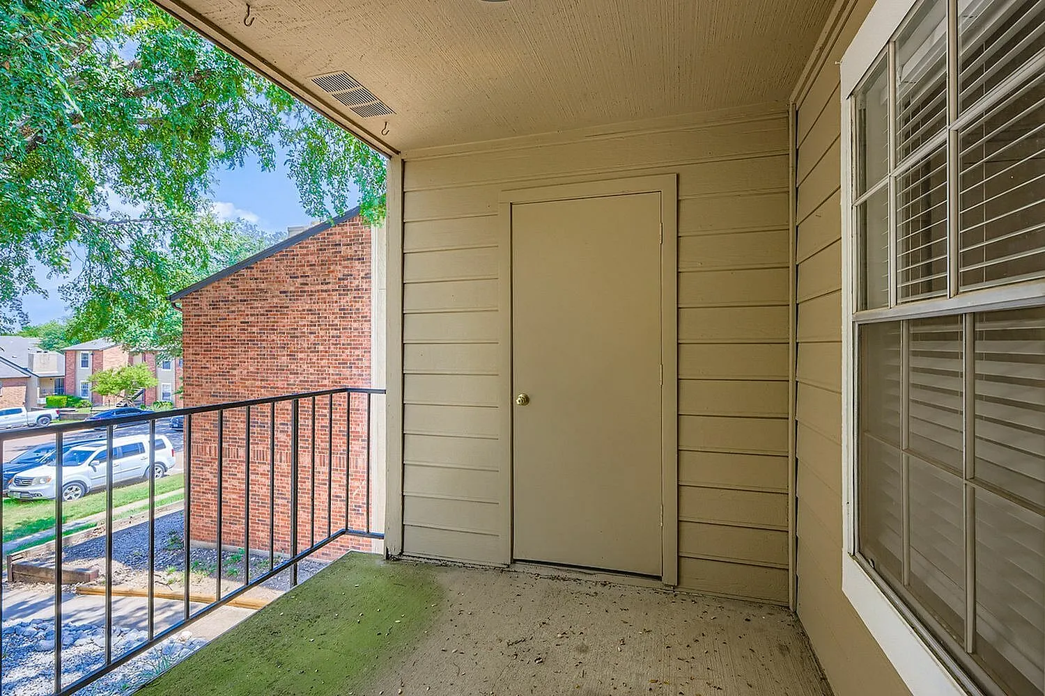 Covered patio, metal railing, cream-colored walls, shuttered windows, brick exterior