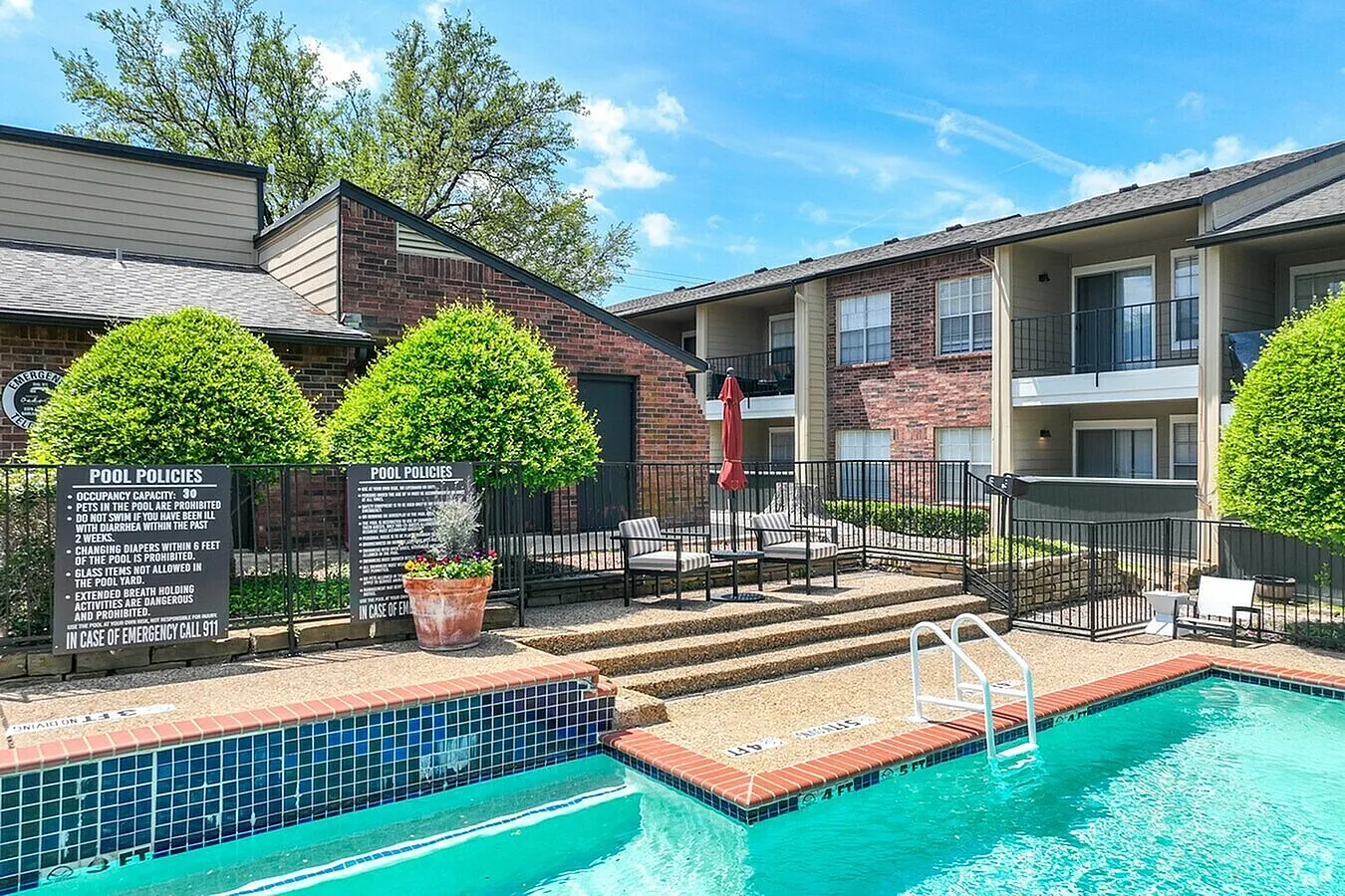 Swimming pool with turquoise water, brick decking, lounge seating, multi-story apartment building