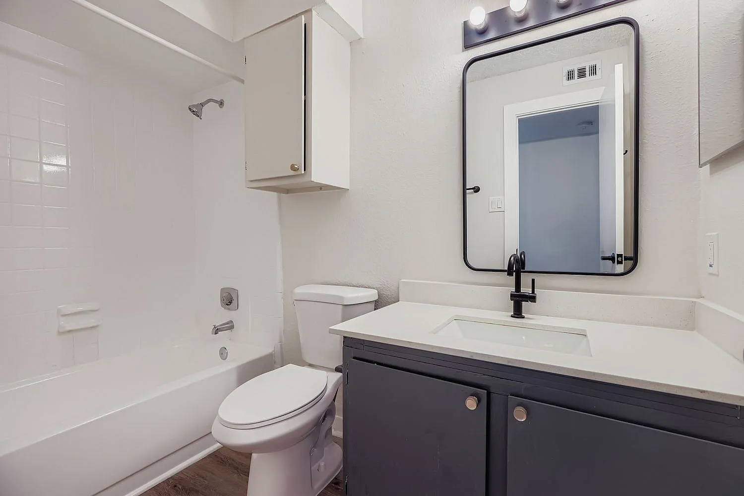 Bathroom, dark vanity, white quartz countertop, framed mirror, toilet, subway tile surround