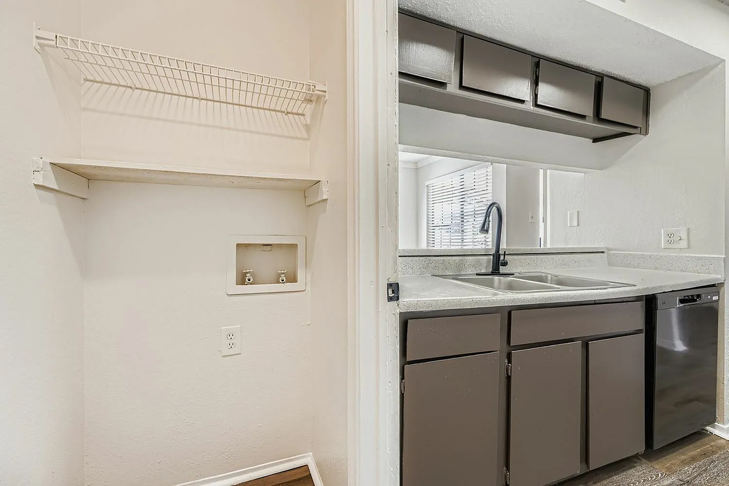 Kitchen with dark cabinetry, quartz countertops, stainless appliances, sink with faucet, open shelving above, utility area with wire shelving and wood-style plank flooring