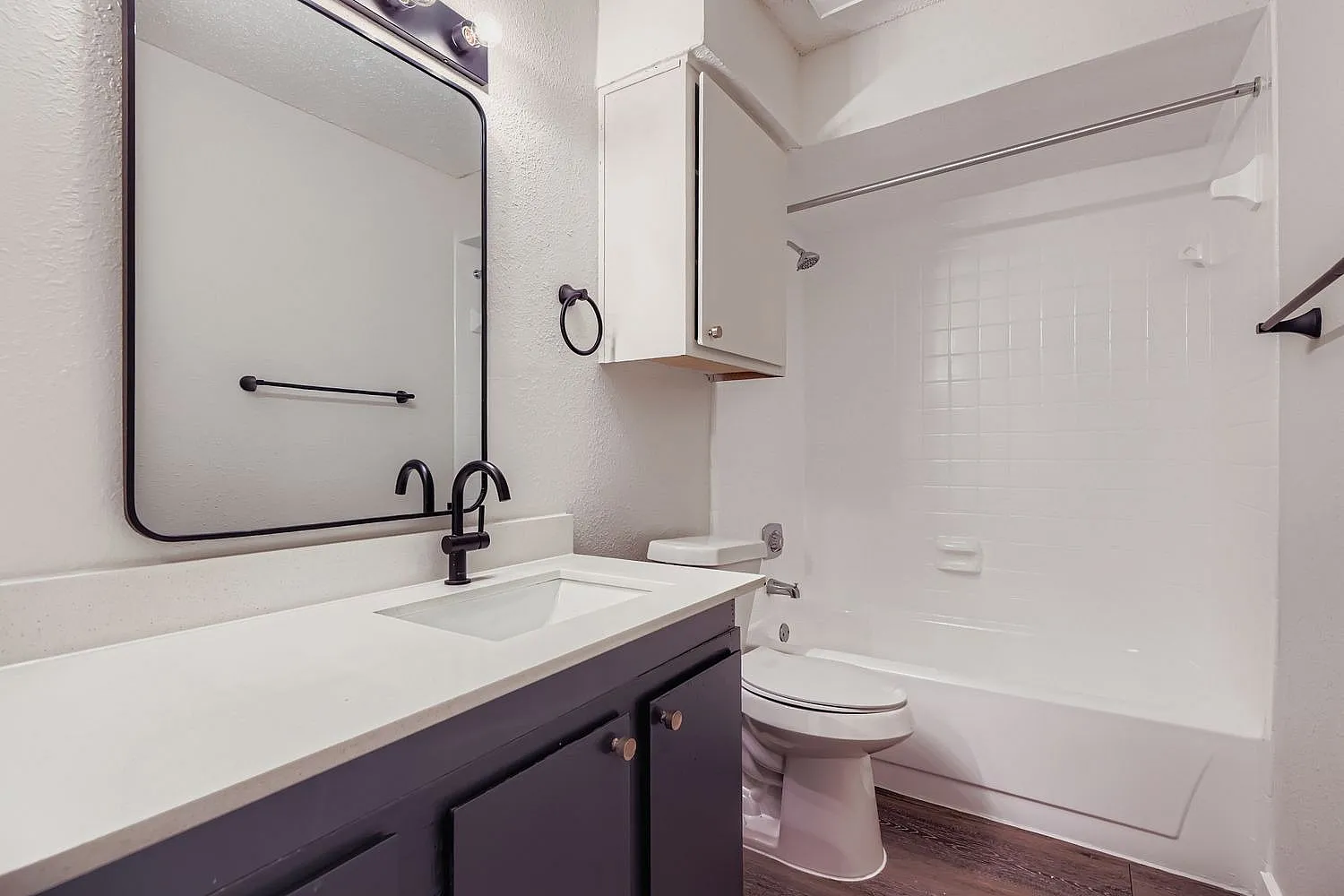 Bathroom, dark vanity cabinetry, white quartz countertops, framed mirror, walk-in shower with white tile