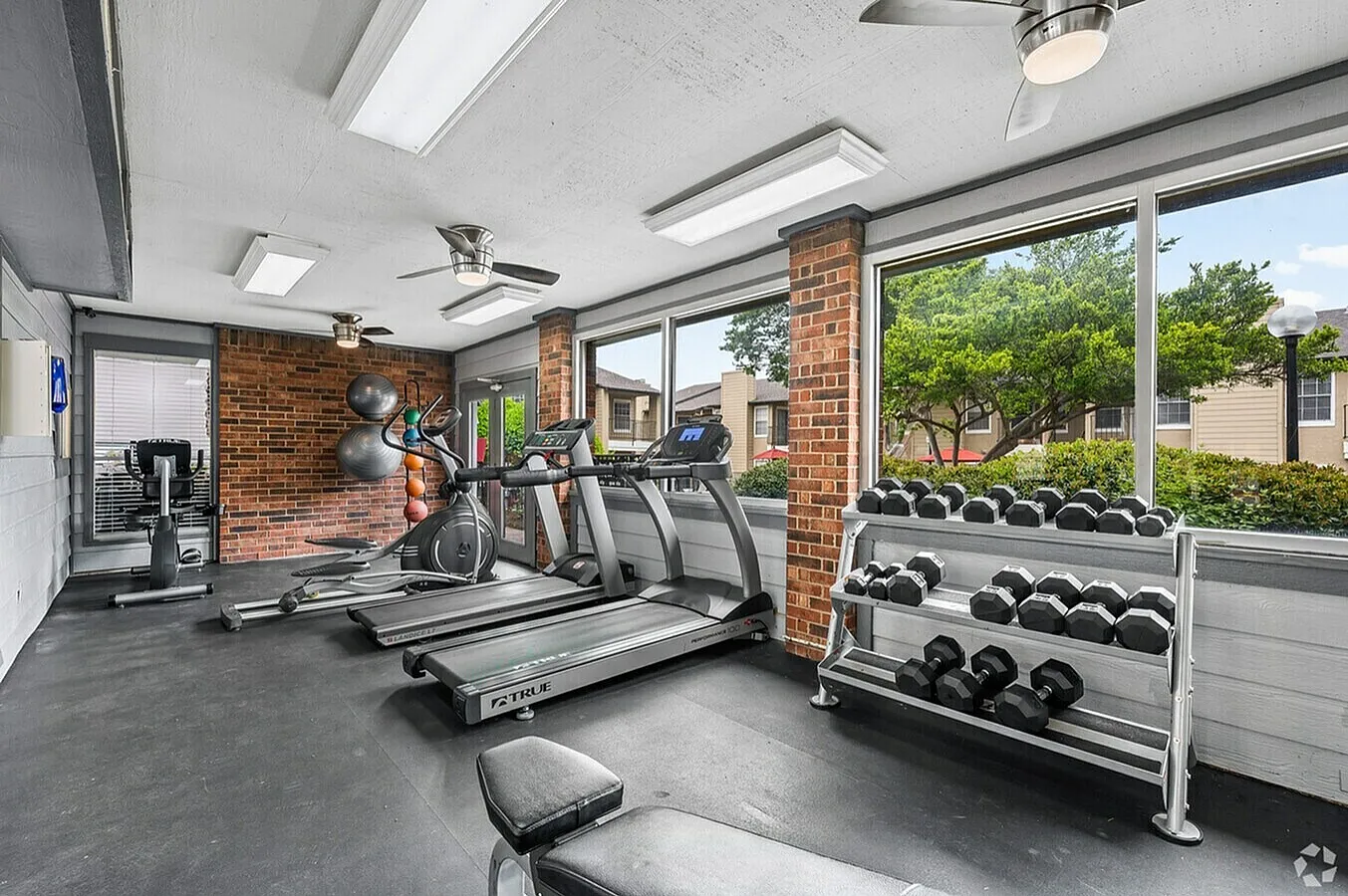 Fitness center, treadmills, ellipticals, dumbbell rack, brick walls, large windows