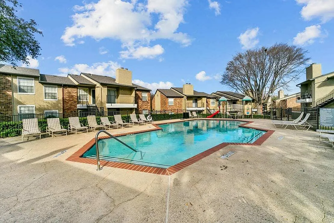 Community pool with clear blue water, lounge seating, brick and tan apartment buildings, mature trees