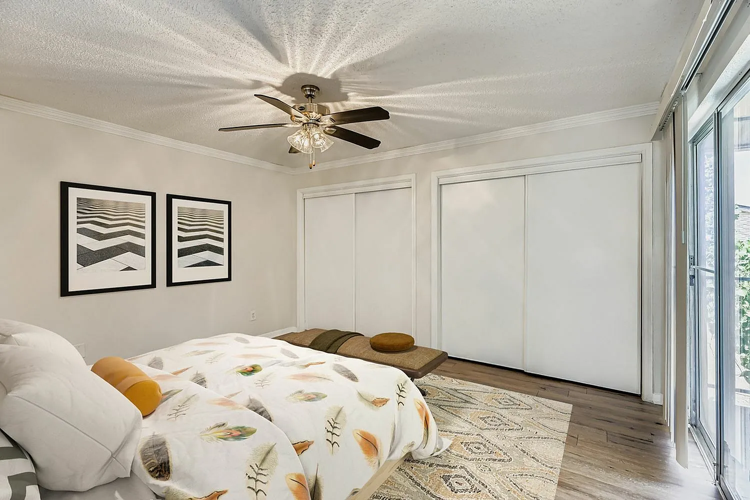 Primary bedroom, wood-style plank flooring, ceiling fan, sliding glass doors, framed artwork