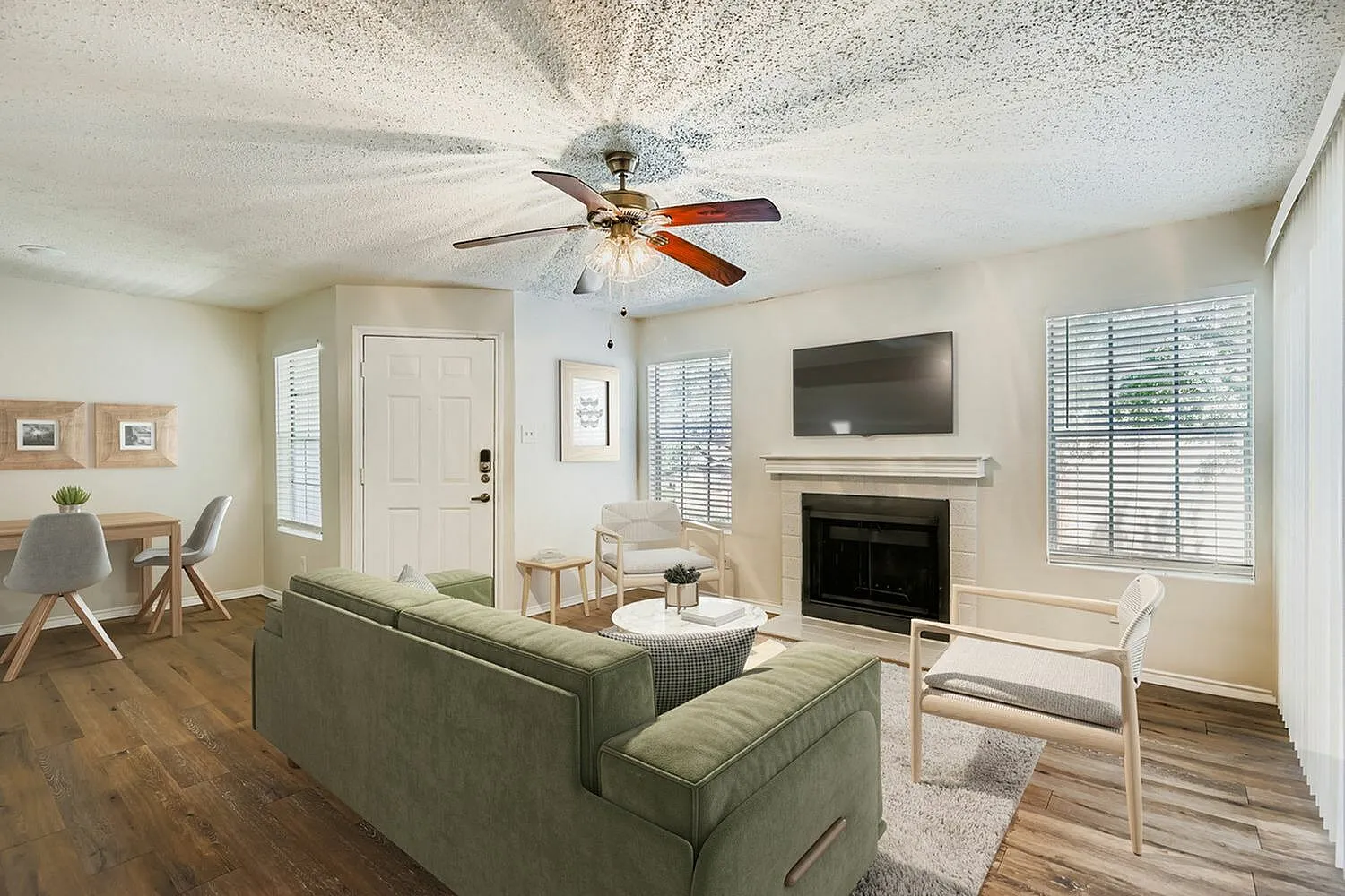 Living room, wood-style plank flooring, green sectional sofa, ceiling fan, fireplace with TV