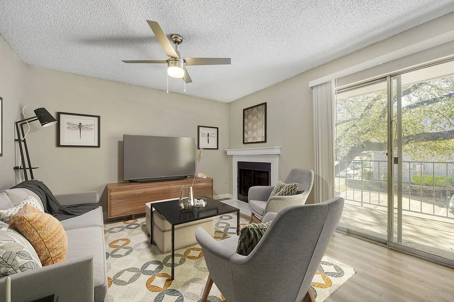 Living room, wood-style plank flooring, ceiling fan, gray seating, sliding glass doors to balcony