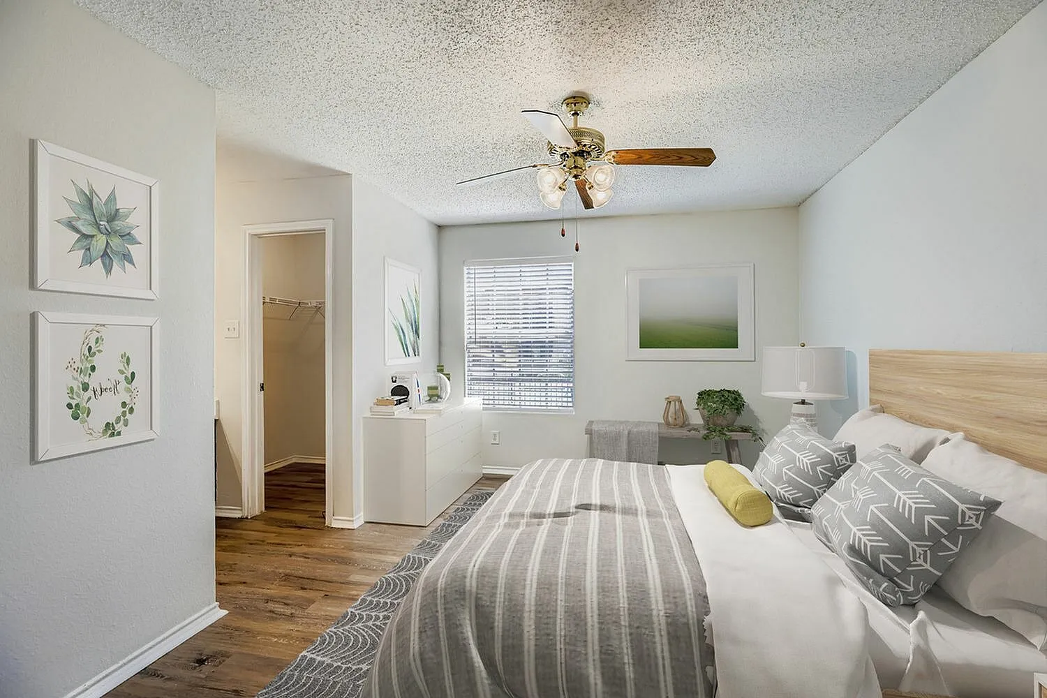 Primary bedroom, wood-style plank flooring, ceiling fan, striped bedding, en suite access