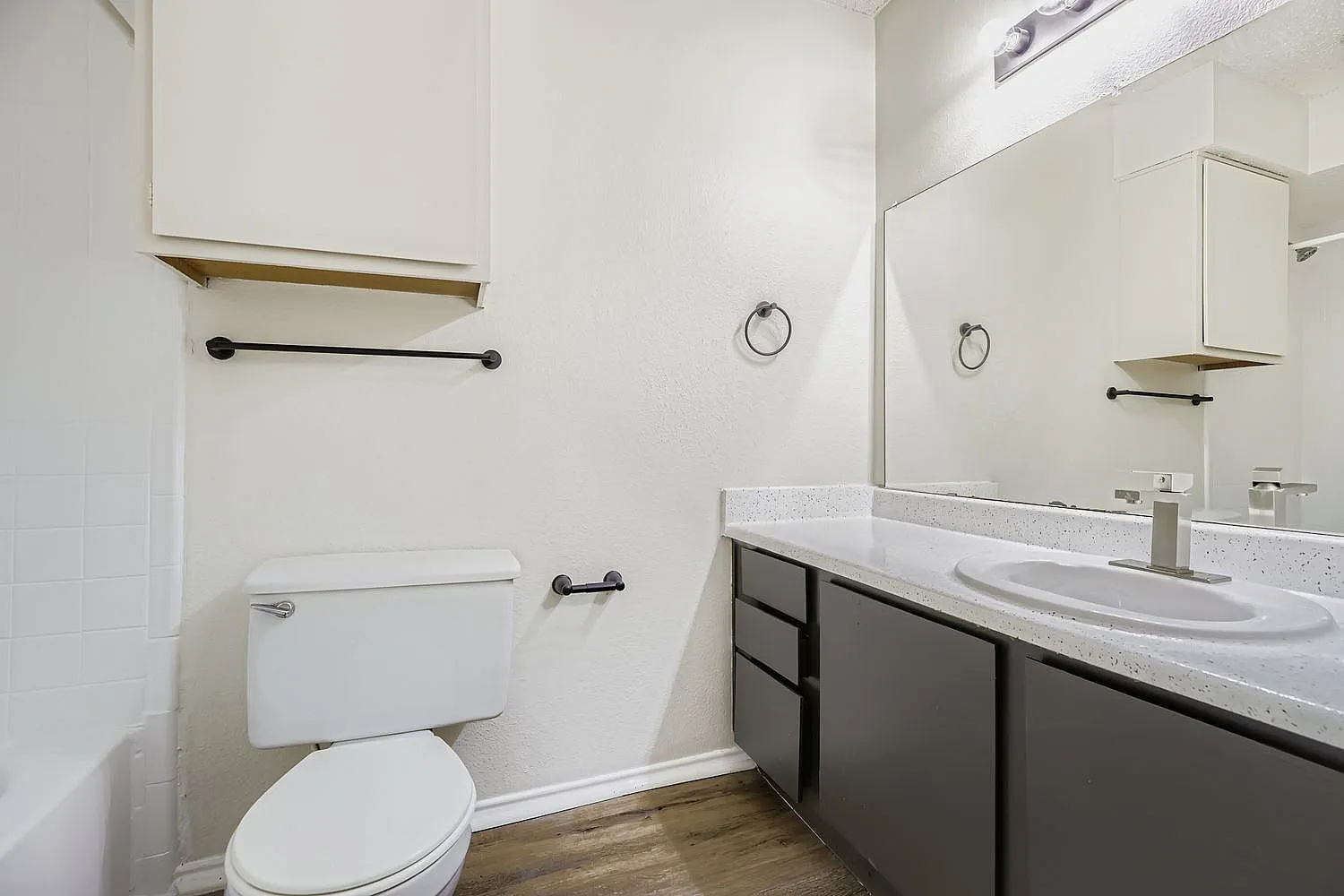 Bathroom, dark cabinetry vanity, white quartz countertops, white subway tile, wood-style plank flooring