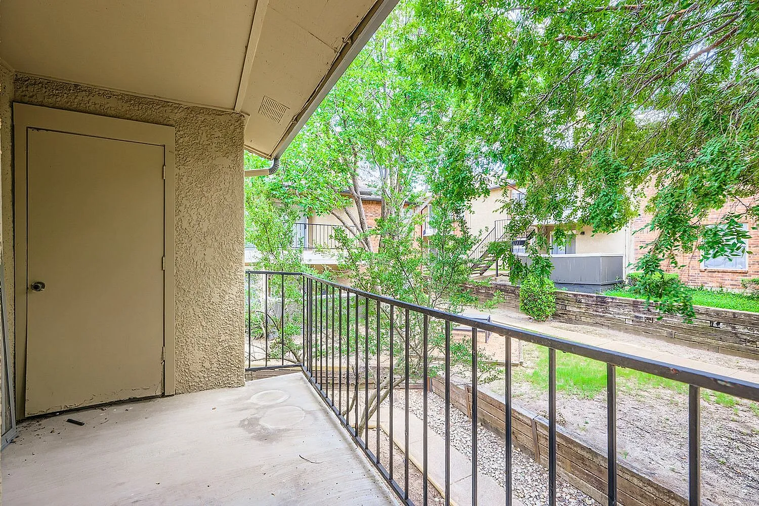 Balcony, concrete flooring, metal railing, cream entry door, ivy covered surroundings