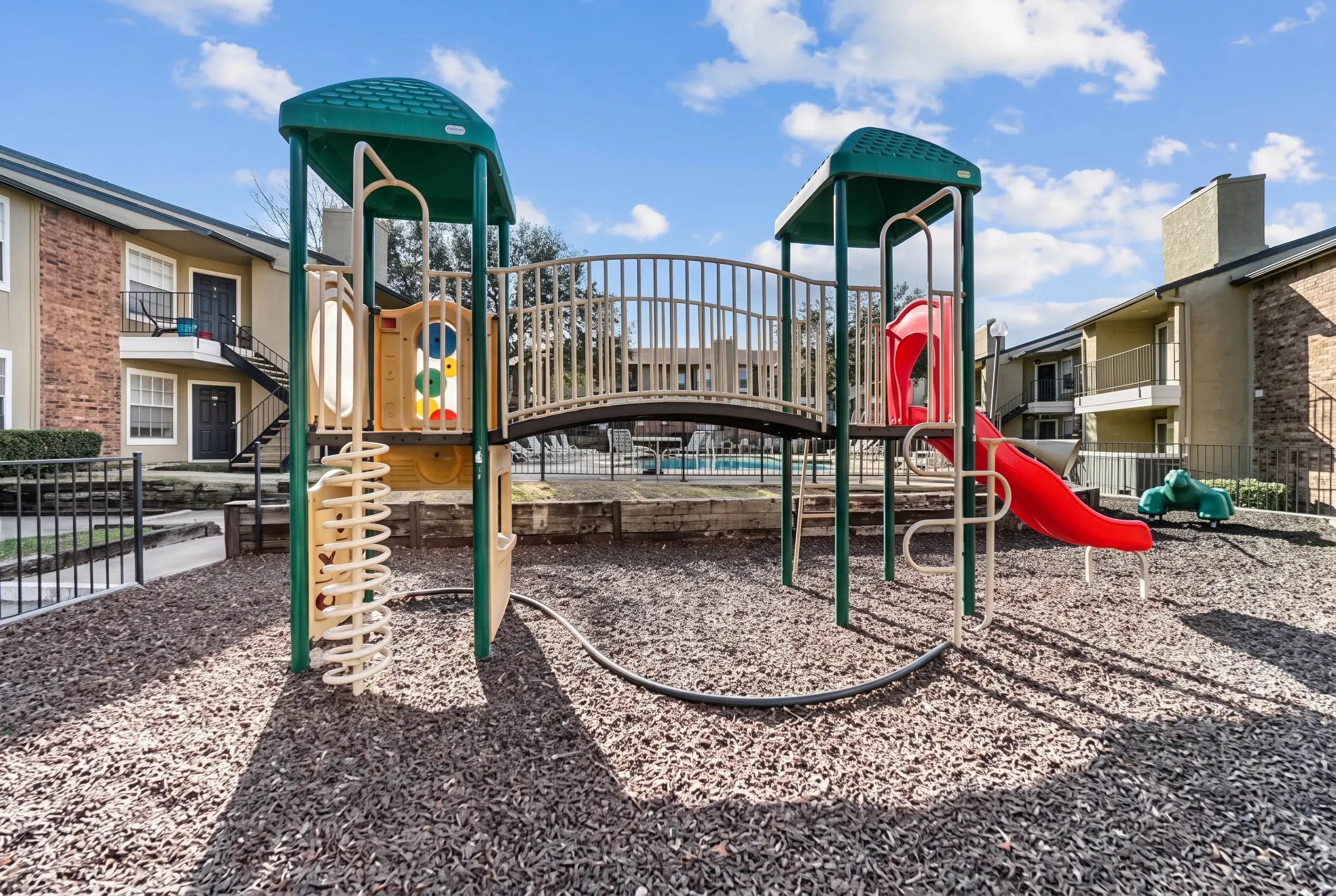 Playground with green canopy structures, climbing walls, red slide, metal bridge walkway