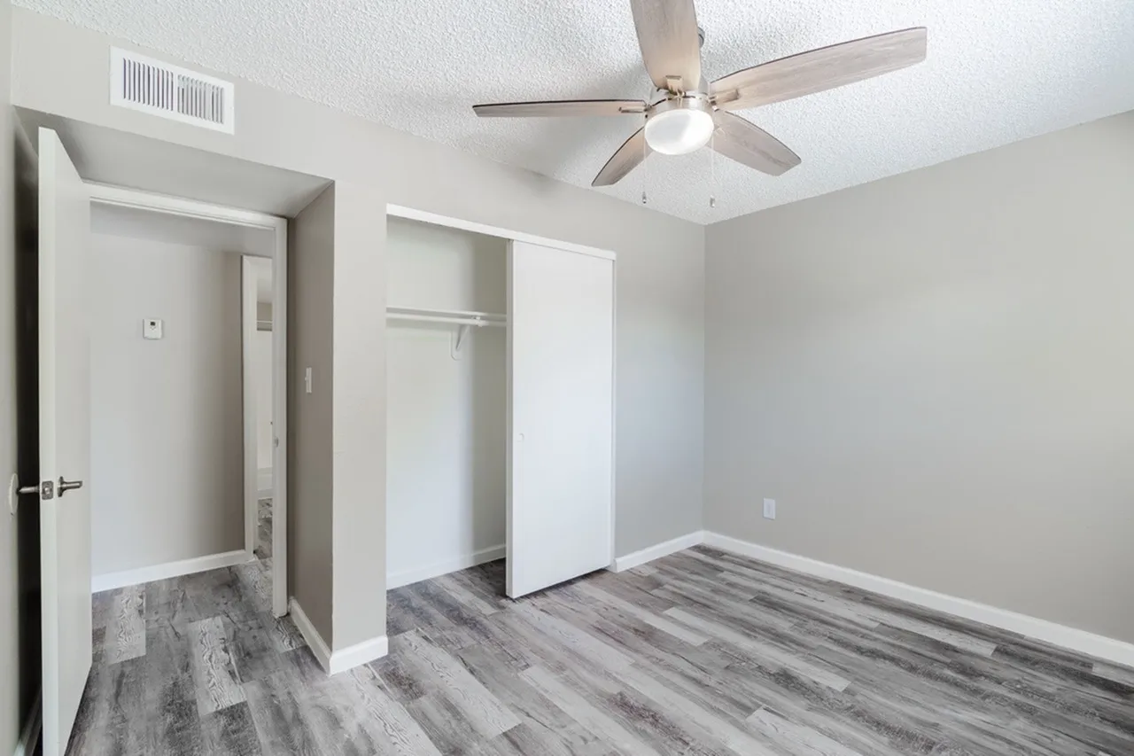 Primary bedroom, wood-style plank flooring, ceiling fan, walk-in closet, ensuite bathroom entry