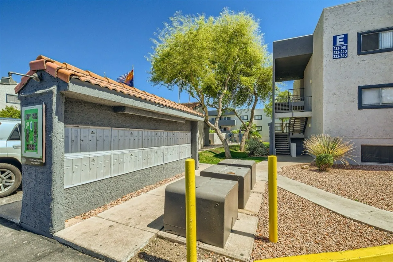 Garage with light gray doors, concrete driveway, yellow bollards, mature tree, modern apartment buildings, Mesa