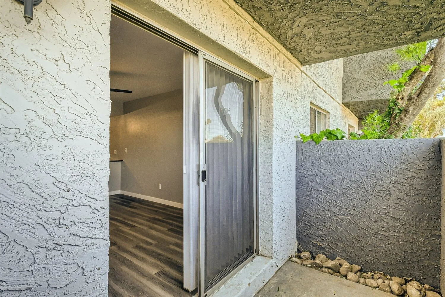 Patio area, sliding glass doors, stucco walls, concrete flooring, planter with greenery
