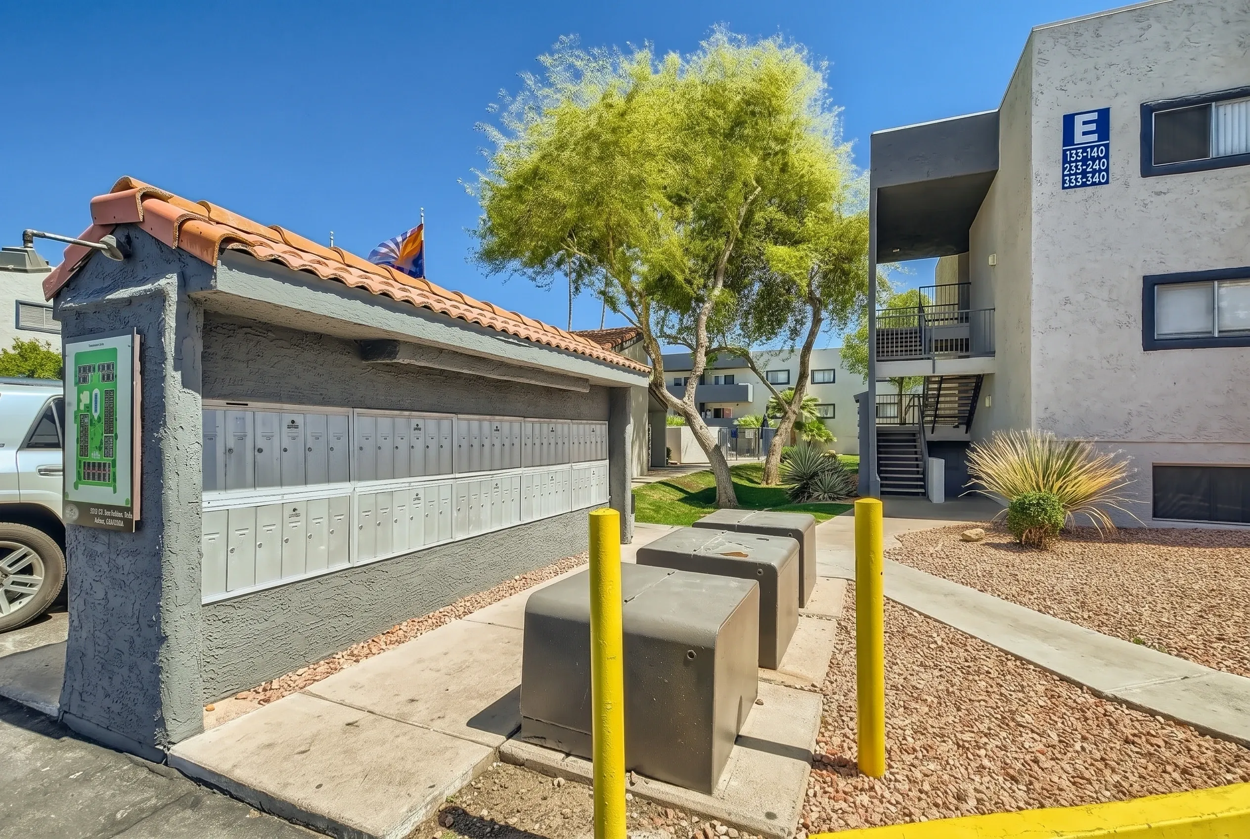 Garage with light gray doors, concrete driveway, yellow bollards, mature tree, modern apartment buildings, Mesa