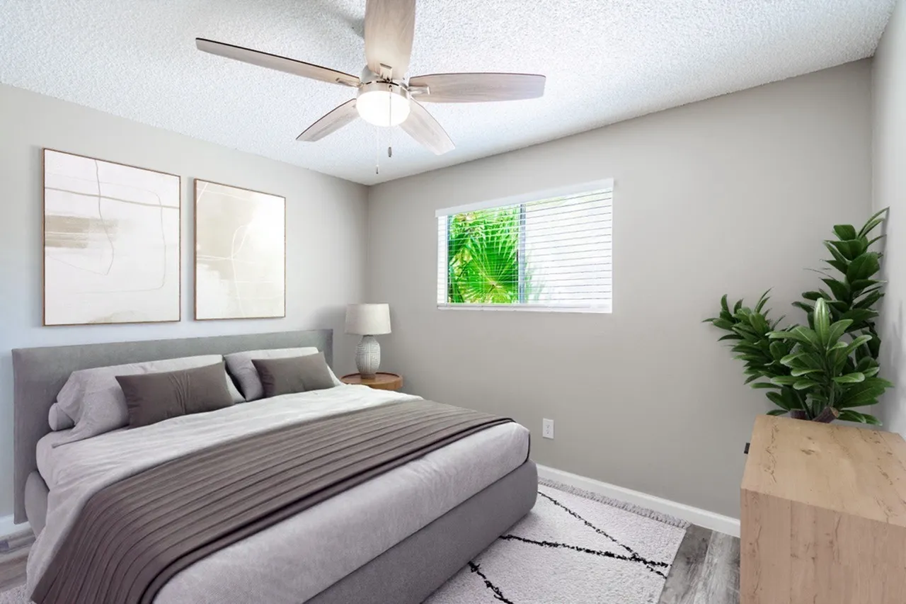 Primary bedroom, gray upholstered headboard, striped bedding, ceiling fan with light, potted plants