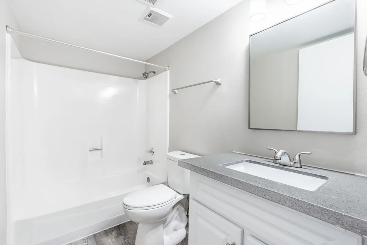 Bathroom, white cabinetry, gray countertops, white ceramic sink, framed mirror