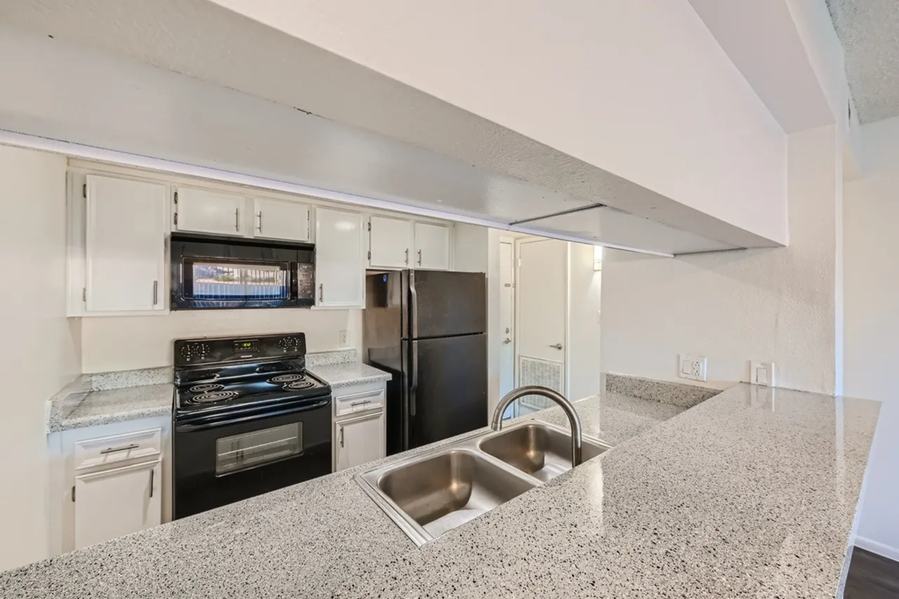 Modern kitchen with white cabinetry, gray speckled countertops, stainless steel double sink, black gas range, black microwave, stainless steel refrigerator, and white ceiling with recessed lighting