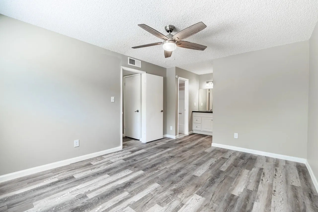 Spacious bedroom featuring gray and white walls, light wood-style vinyl plank flooring, a brushed nickel ceiling fan with integrated lighting, white closet doors, and multiple electrical outlets