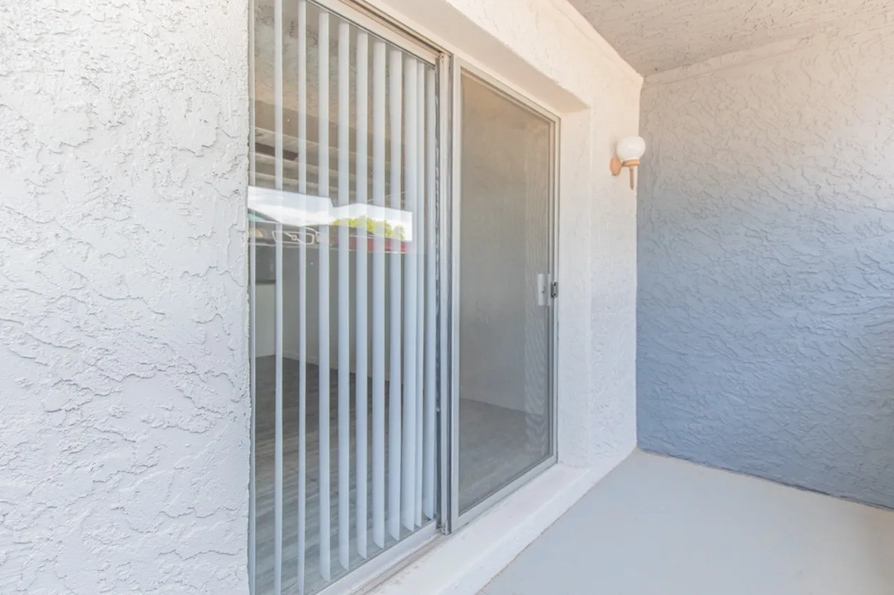 Balcony, vertical blinds, sliding glass door, textured walls, white plank flooring