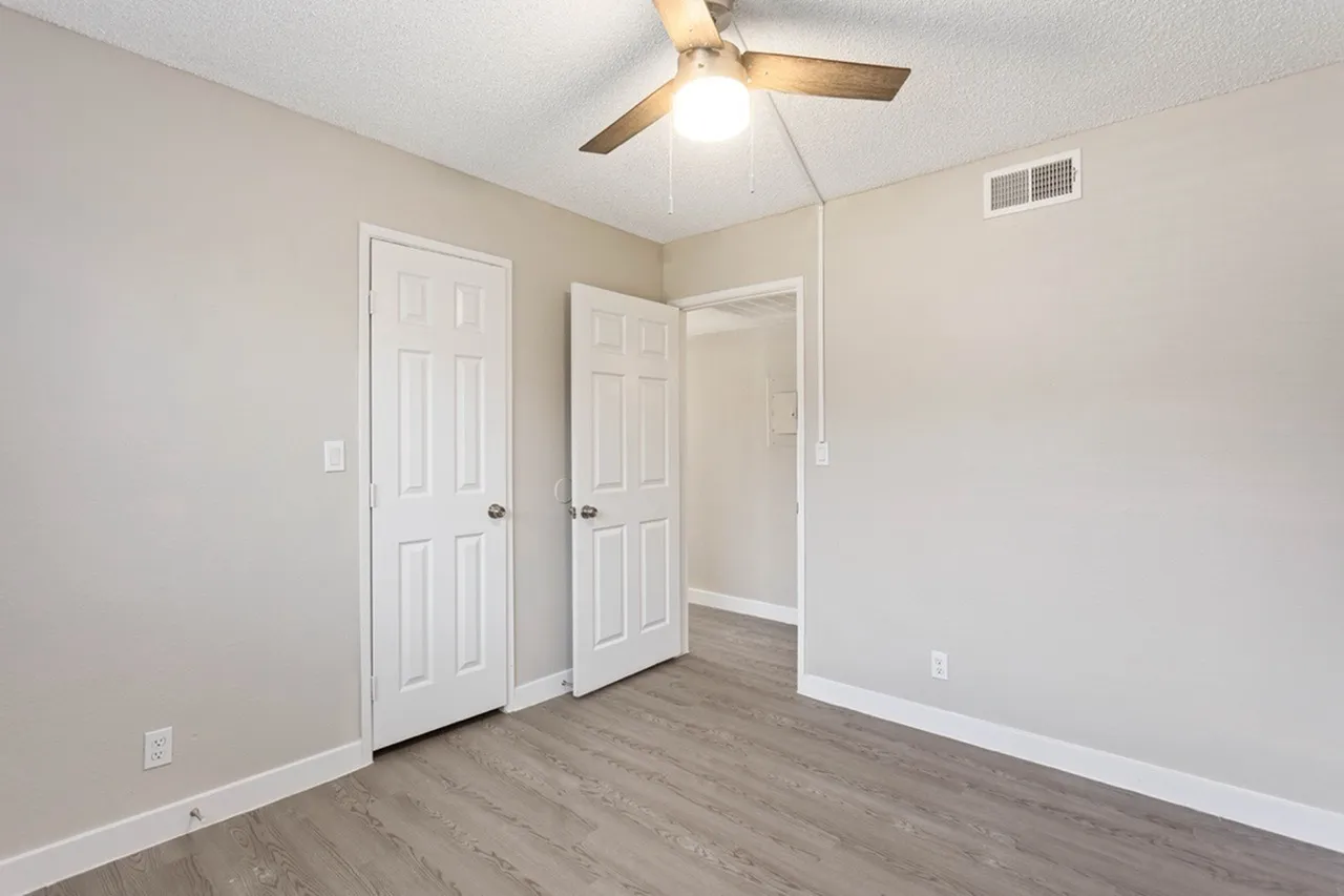 Bedroom, double closets with white doors, wood-style plank flooring, ceiling fan