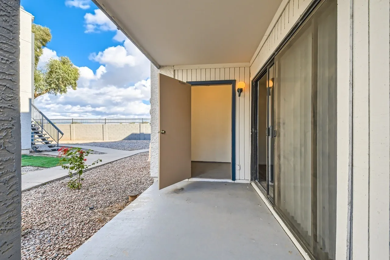 Covered patio, concrete flooring, yellow entry door, stainless railings, landscaped yard view