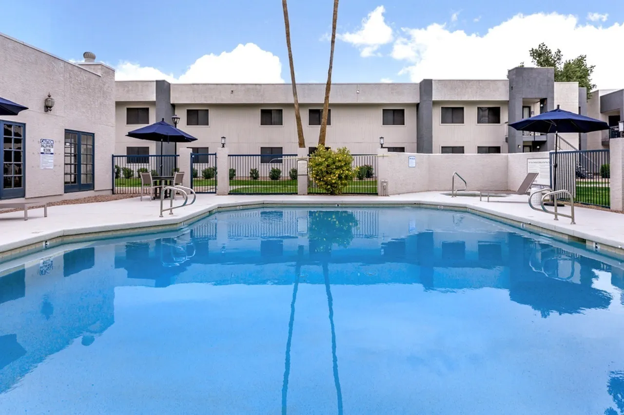 Swimming pool, blue water, lounge chairs, blue umbrellas, residential buildings