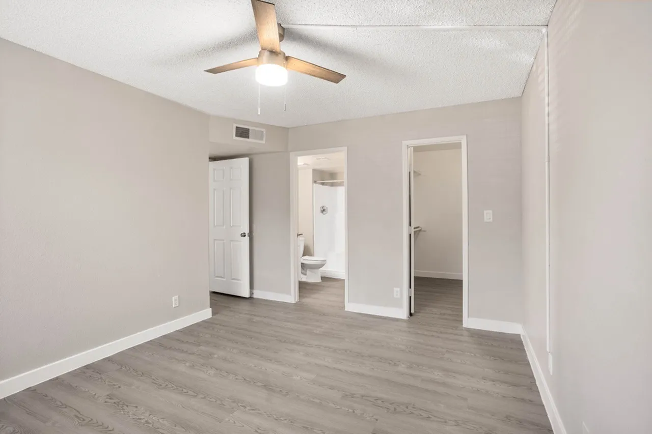 Primary bedroom, wood-style plank flooring, ceiling fan with light, open doorways to en-suite bathroom