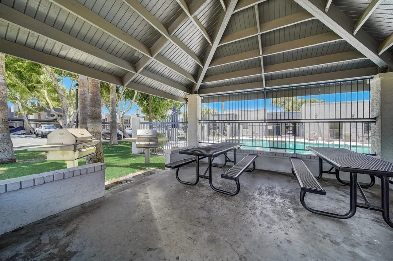 Covered picnic pavilion, metal picnic tables, concrete flooring, pool view with safety fencing