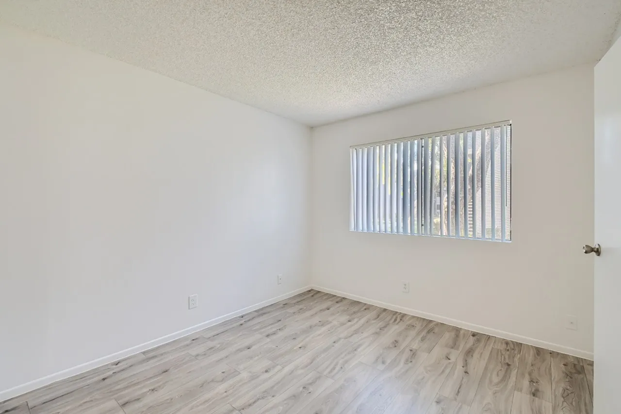 Bedroom, wood-style plank flooring, vertical window blinds, textured ceiling