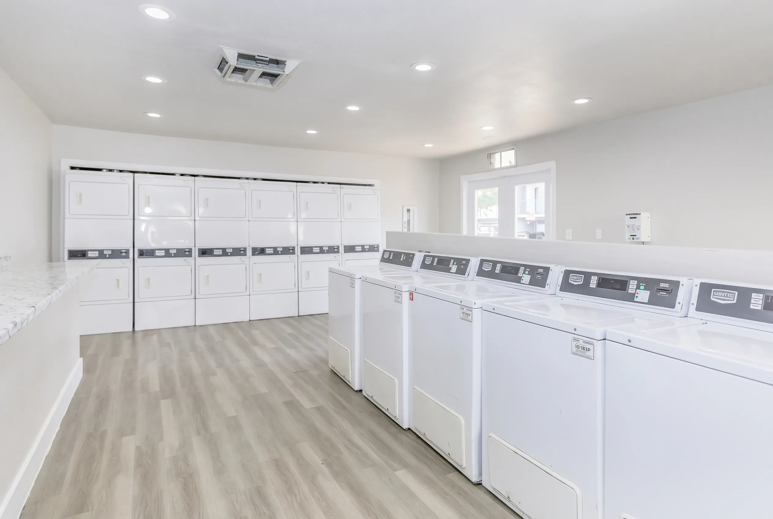 Laundry room, white front-load washers and dryers, wood-style plank flooring, recessed lighting