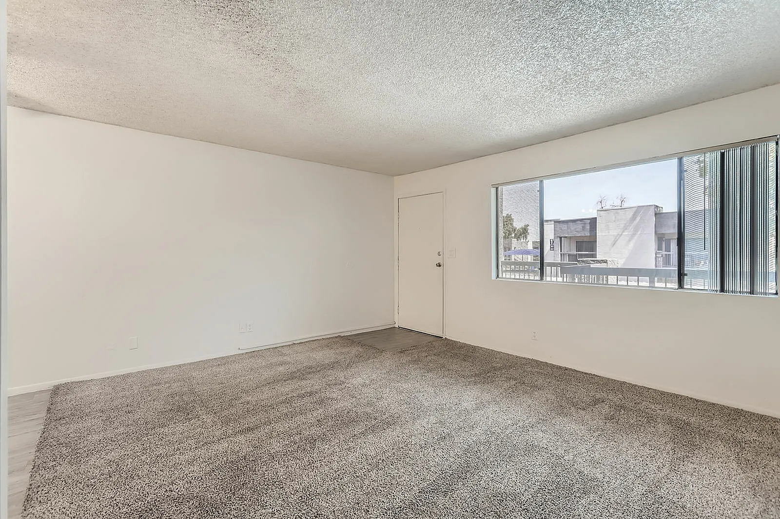 Living room, gray carpet flooring, large windows, textured ceiling