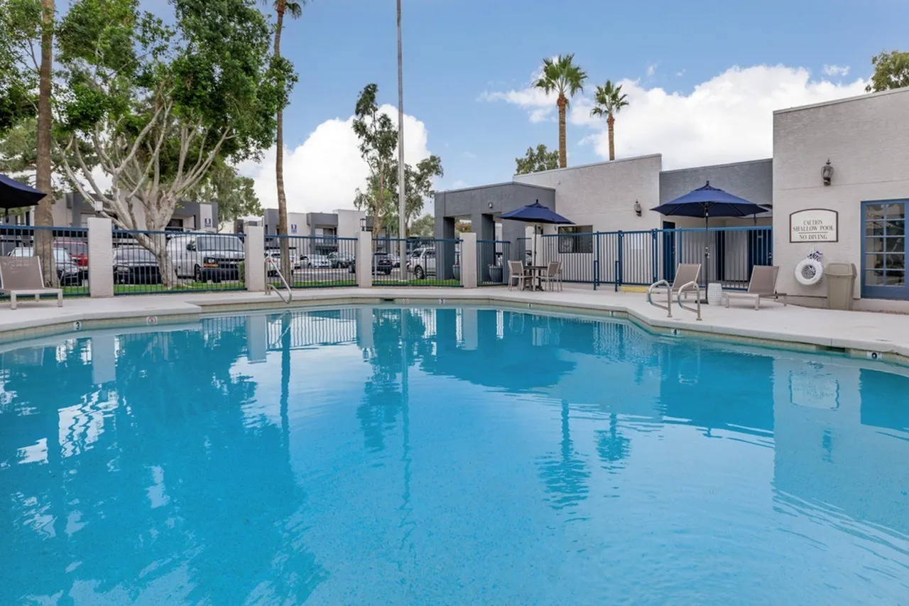 Resort-style swimming pool, blue umbrellas, lounge seating, white building structures, palm trees