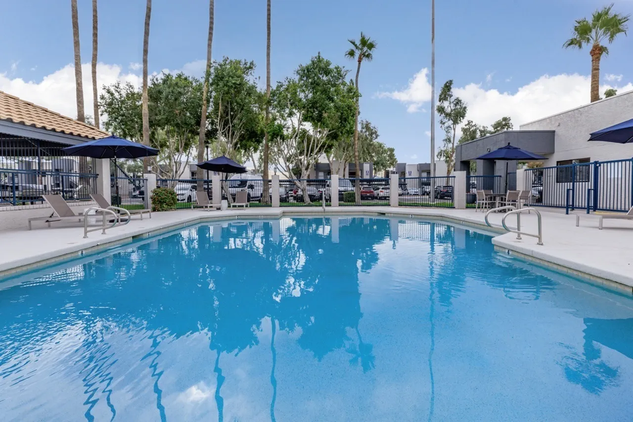 Resort-style swimming pool, clear blue water, palm trees, lounge chairs, umbrellas, buildings