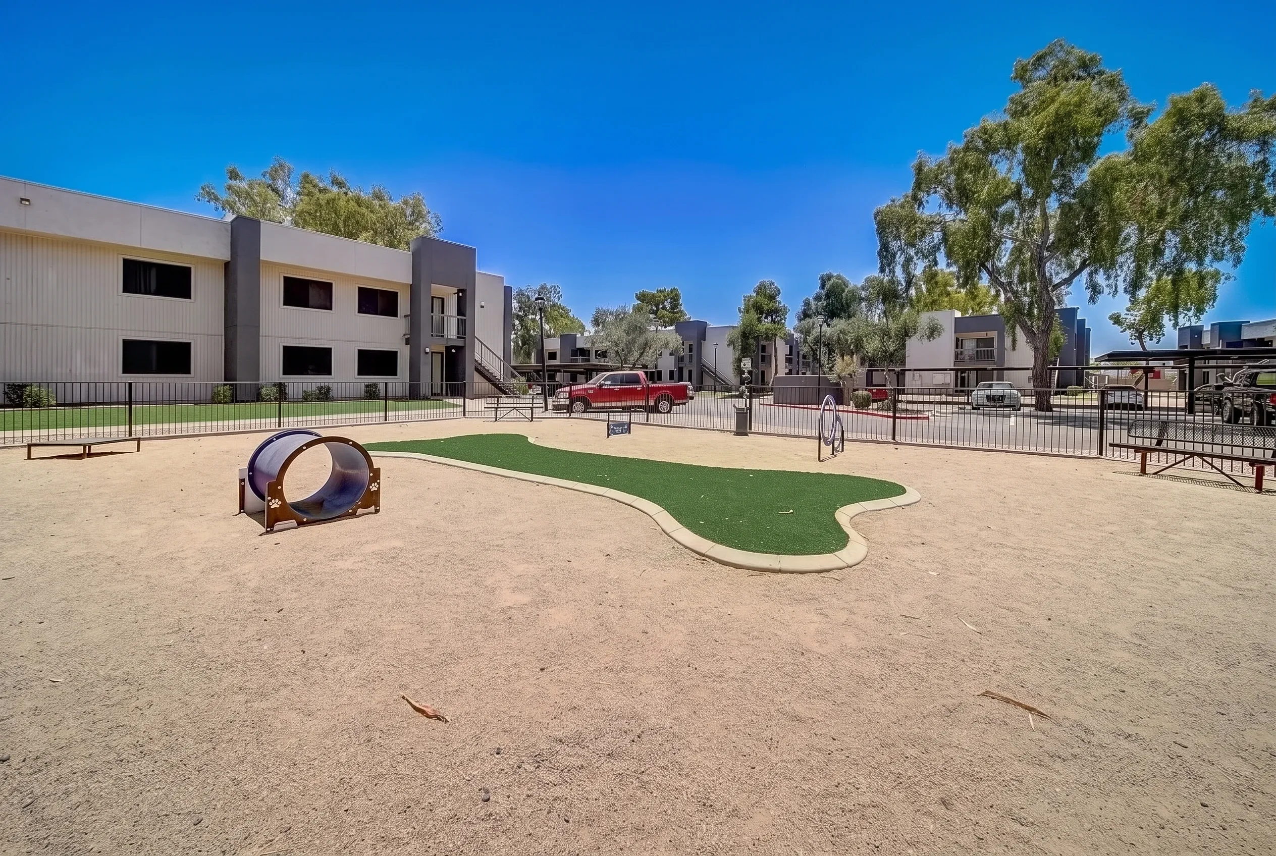 Dog park, artificial turf area, tunnel agility equipment, shade trees, residential buildings