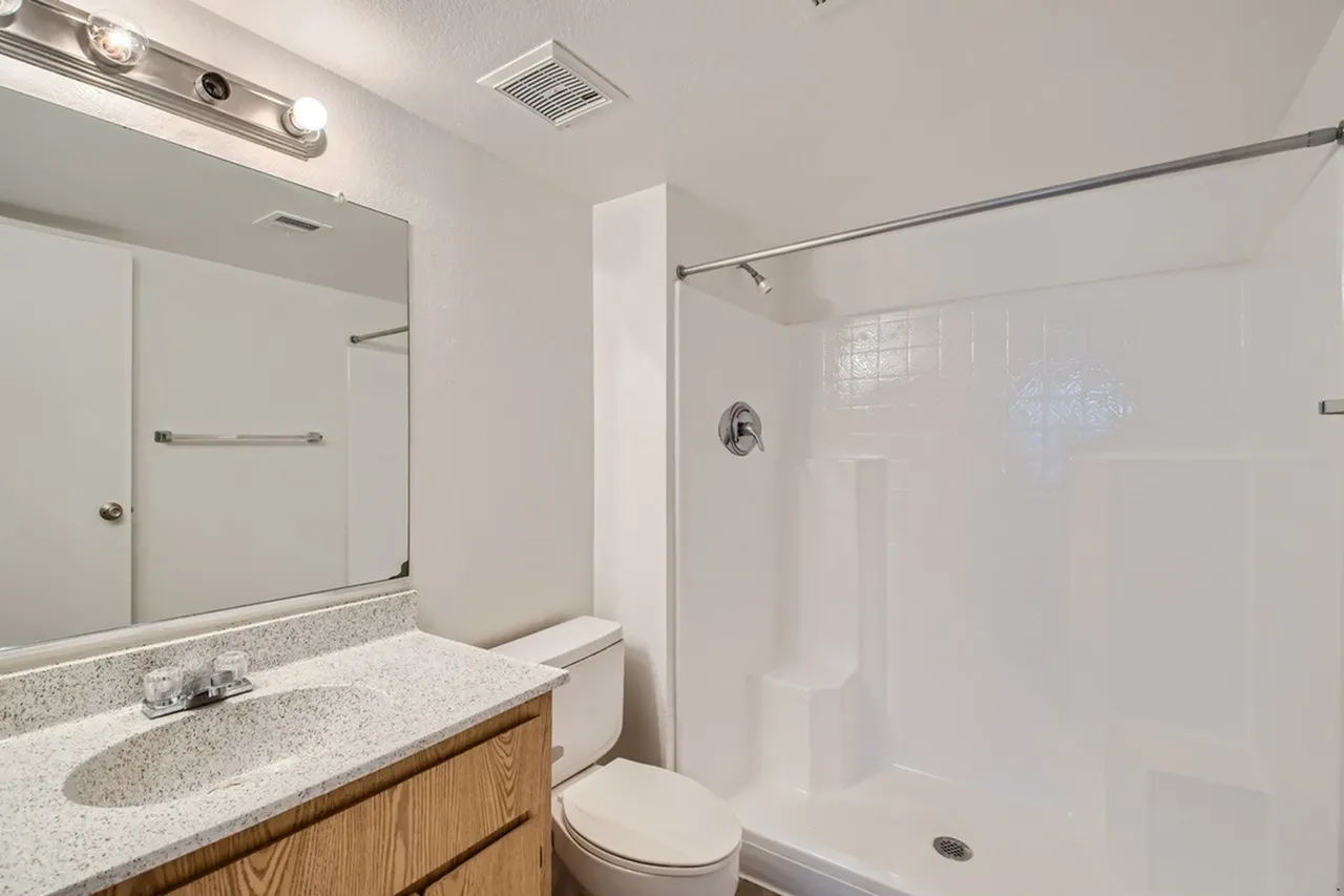 Bathroom, quartz countertop, wood cabinetry, framed mirror, glass shower enclosure