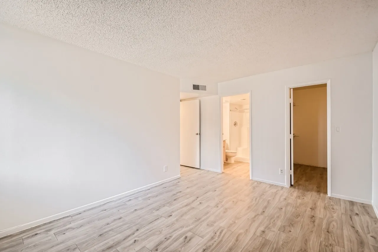 Bedroom, wood-style plank flooring, white walls, multiple doors, ceiling vent