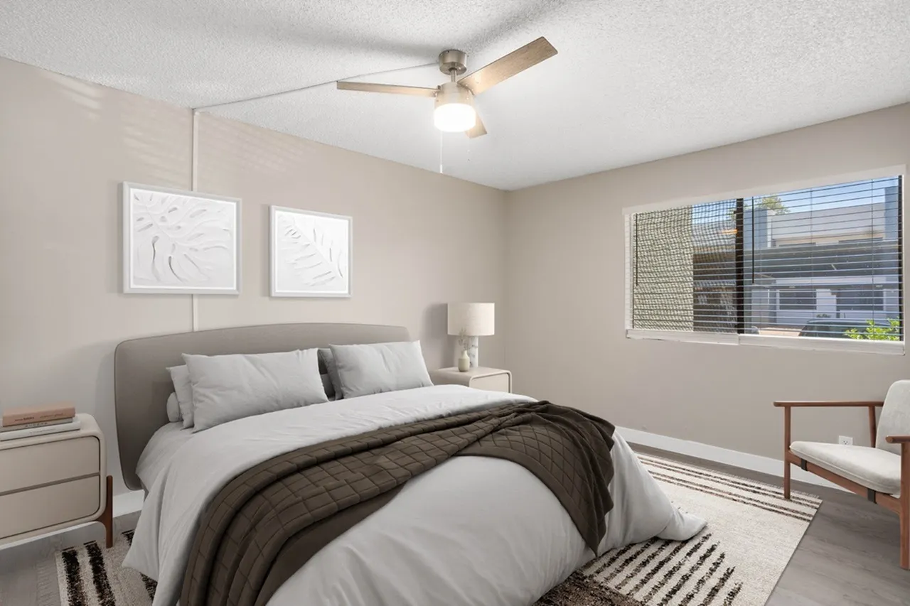 Primary bedroom, gray upholstered headboard, ceiling fan, striped area rug, bedside table with lamp