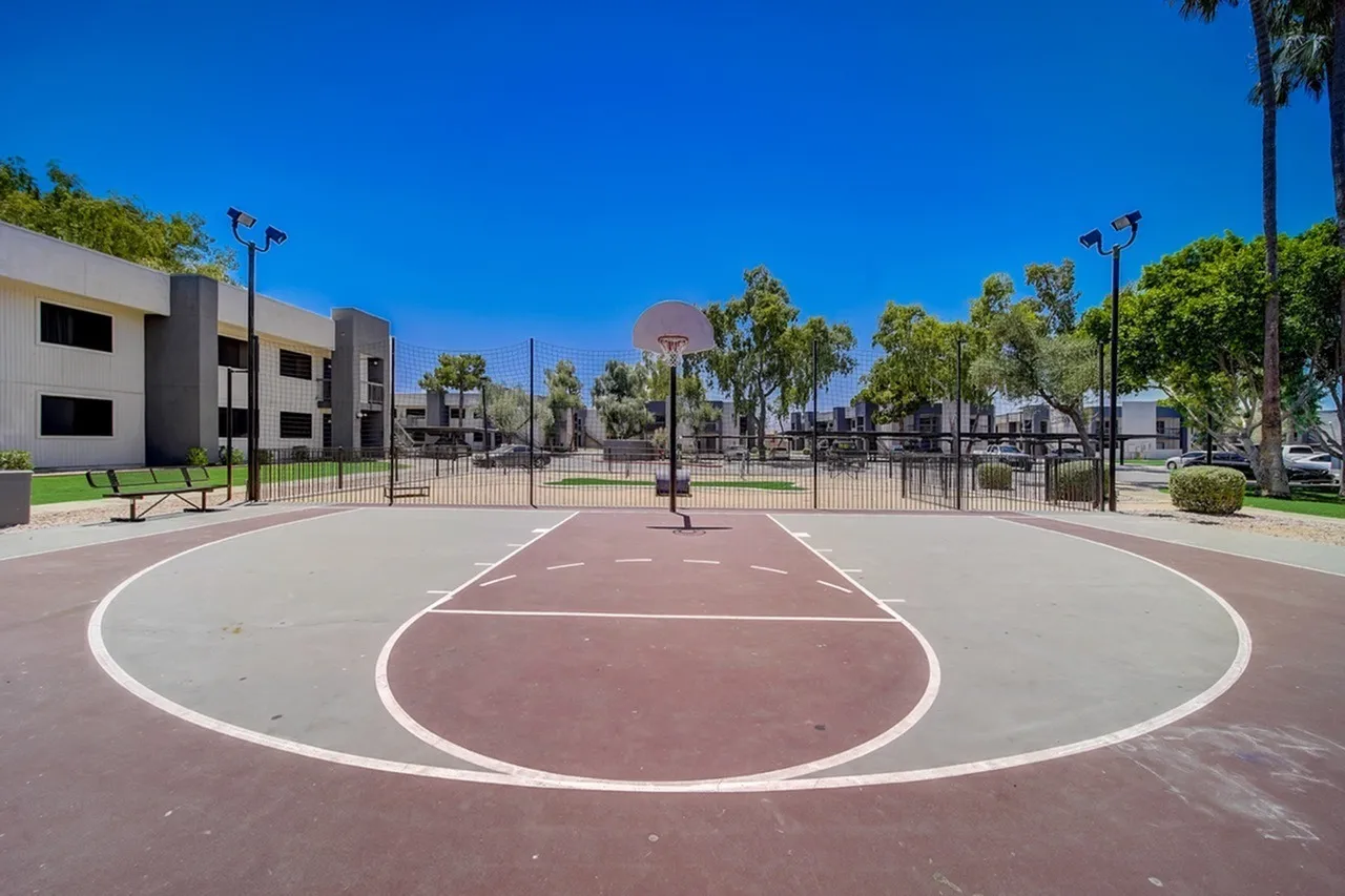 Outdoor basketball court, red and gray surface, white line markings, apartment building, palm trees