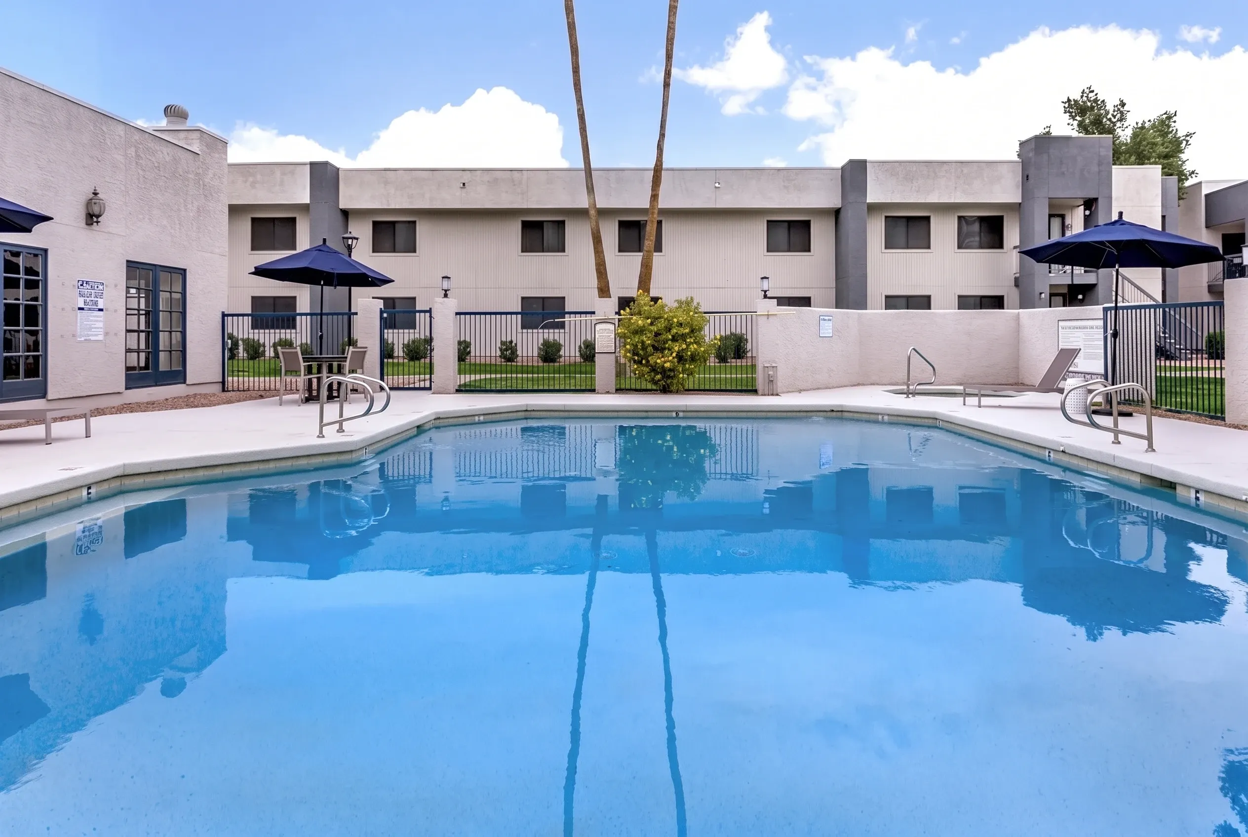 Swimming pool, blue water, lounge chairs, blue umbrellas, residential buildings